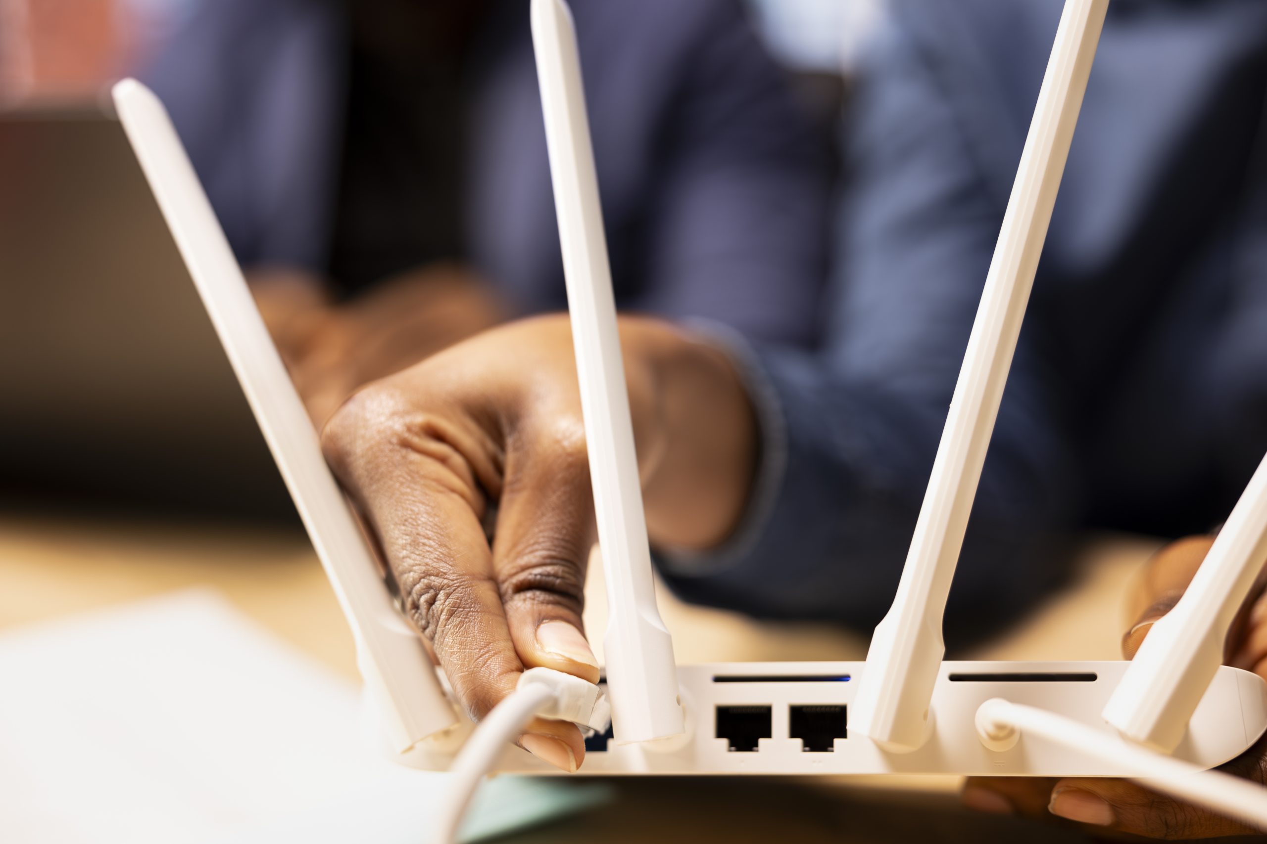 Young black woman pulling out the LAN cable from the modem while her boyfriend reads a technical manual on laptop for troubleshooting. Wi-Fi reset to fix connectivity issues. Close up.